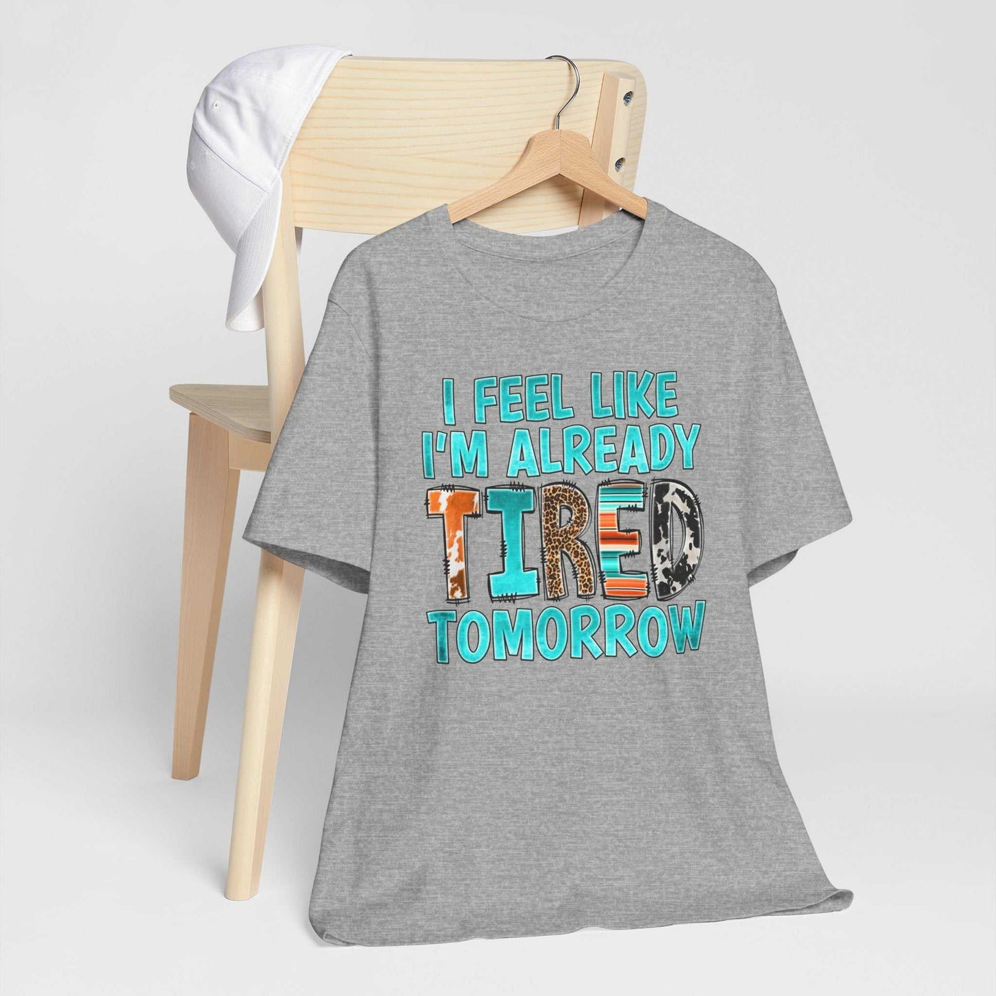 T-Shirt with "I Feel Like I'm Already Tired Tomorrow" phrase, promoting mental health awareness, in bold, colorful letters on soft gray fabric.
