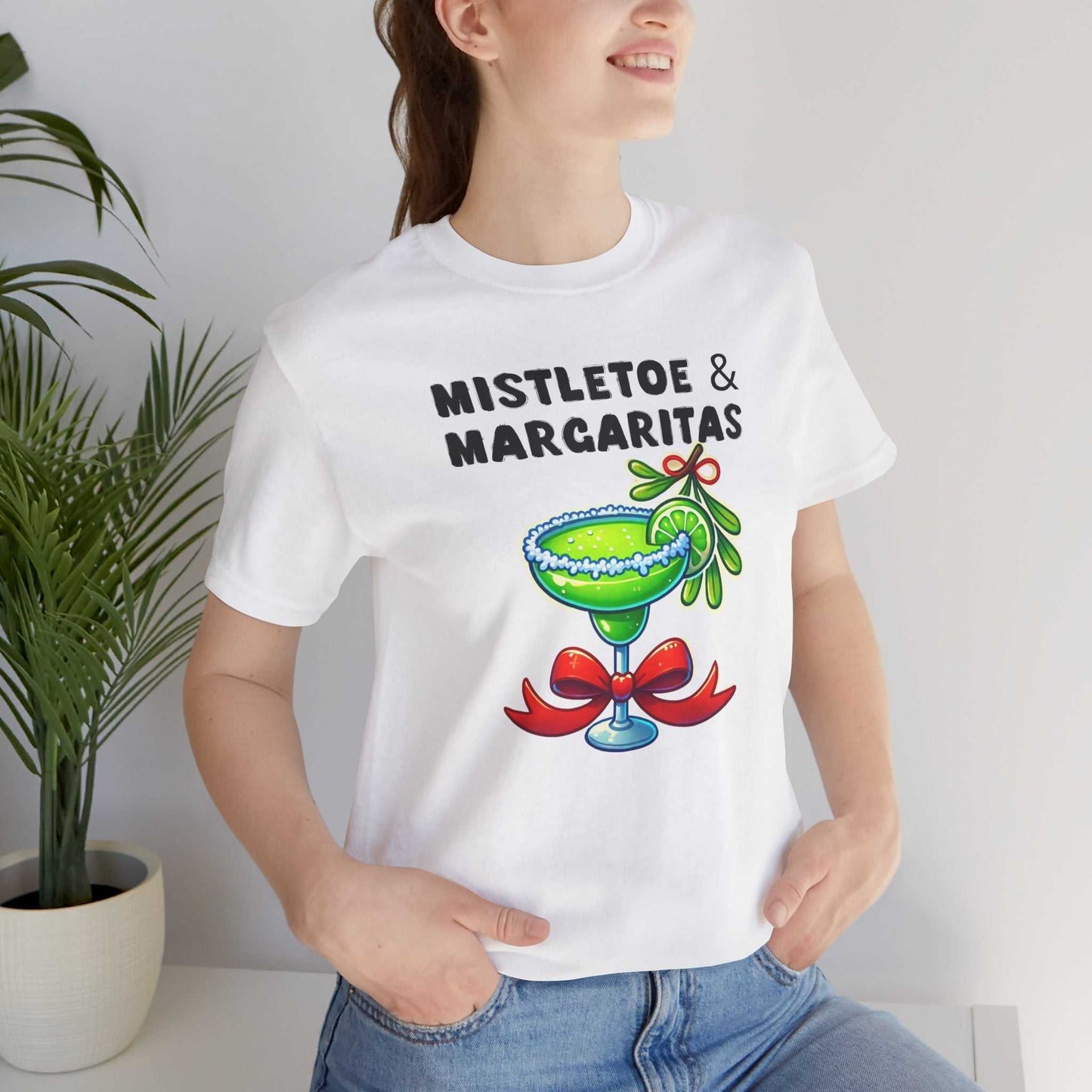 Woman wearing a white unisex t-shirt with "Mistletoe and Margaritas" text and festive margarita graphic for holiday cheer.