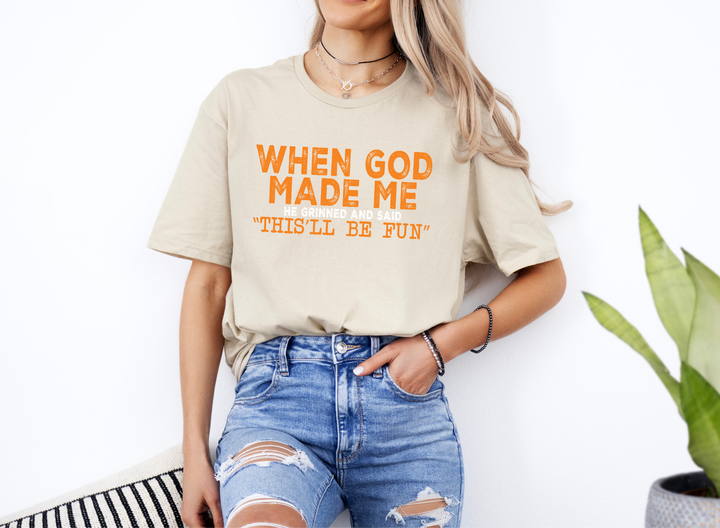 Unisex beige softstyle t-shirt with orange "When God Made Me" graphic print worn with ripped blue jeans