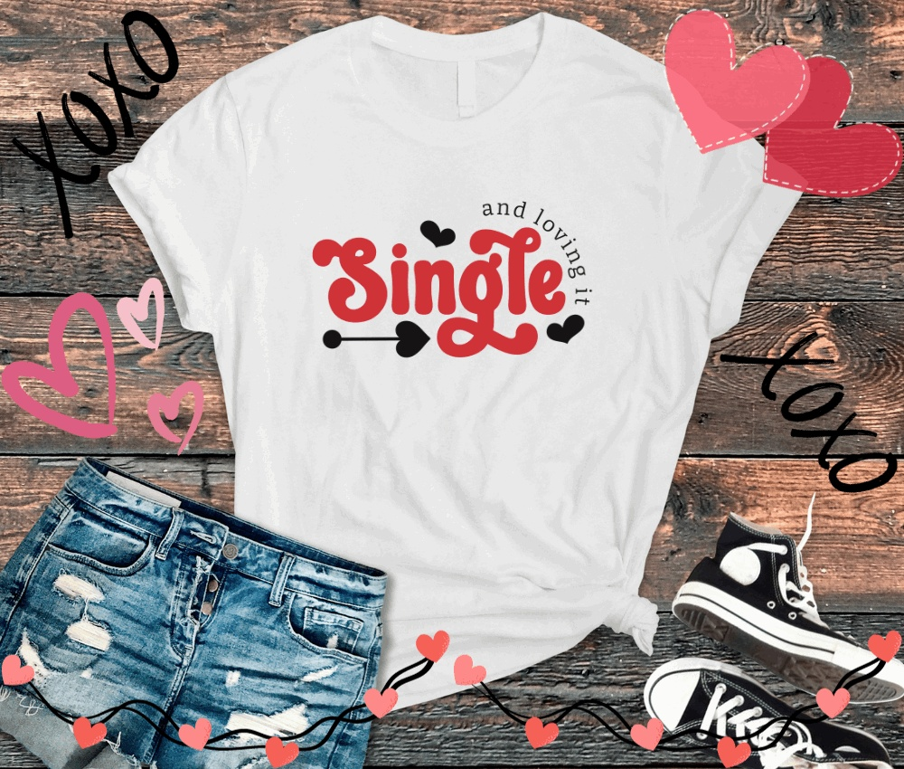 White anti valentine t-shirt with "Single and loving it" text, paired with denim shorts and black sneakers on wooden background