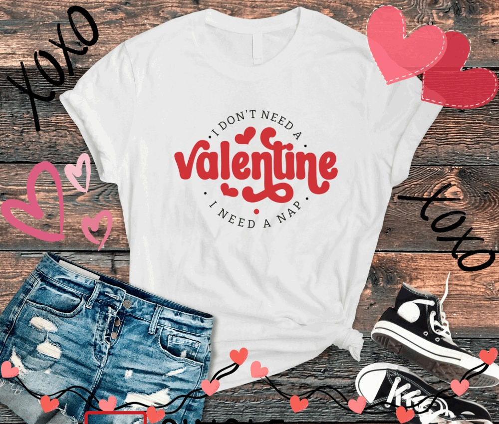 Anti-Valentine T-shirt with "I Don't Need A Valentine, I Need A Nap" text, styled with casual denim shorts and sneakers, surrounded by heart and "XOXO" doodles.