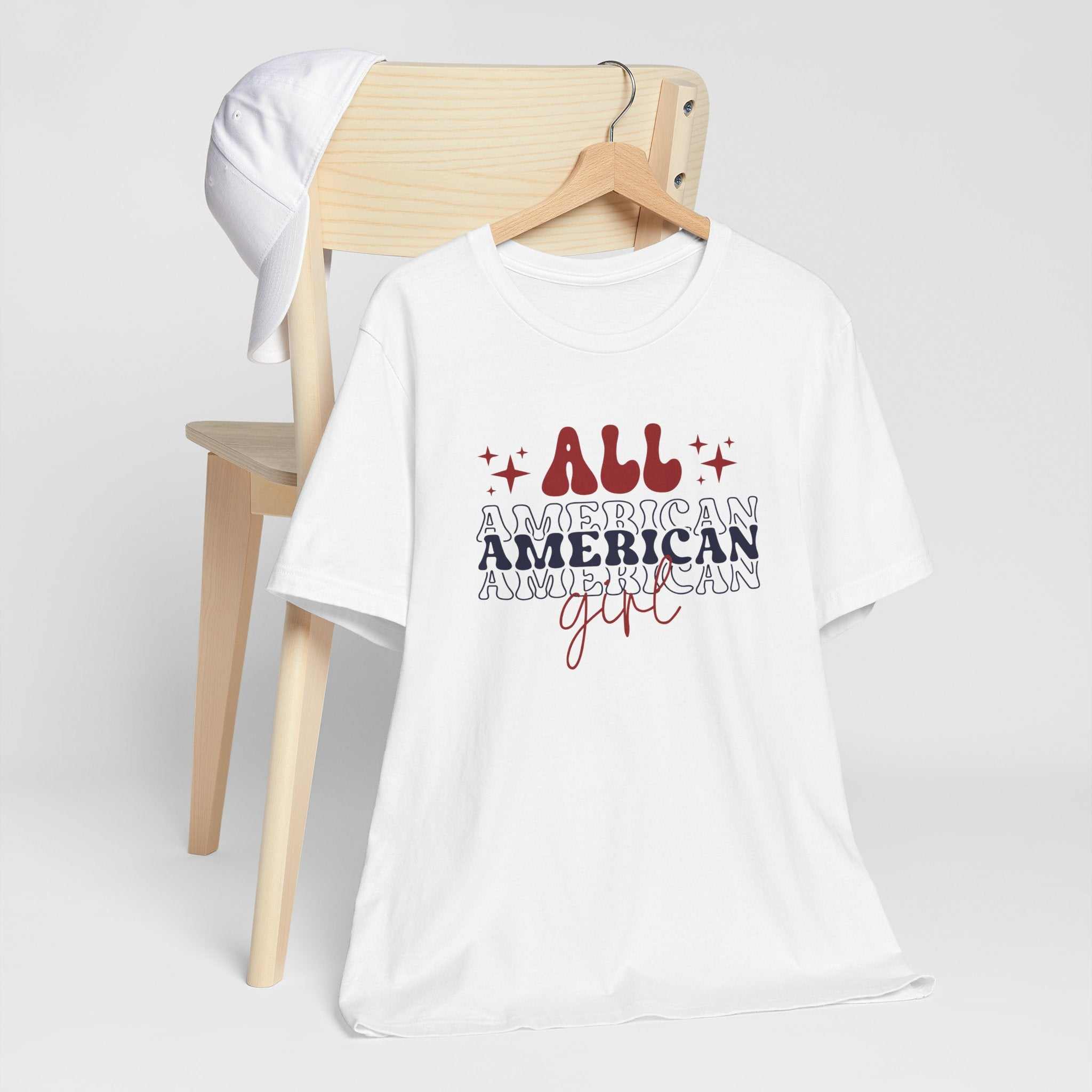 American Girl Independence Day T-Shirt with red, white, and blue graphics on a hanger.