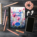 Motivational Journal "Bloom with Purpose" with pink floral cover, personalized name, and surrounding writing accessories on wooden surface