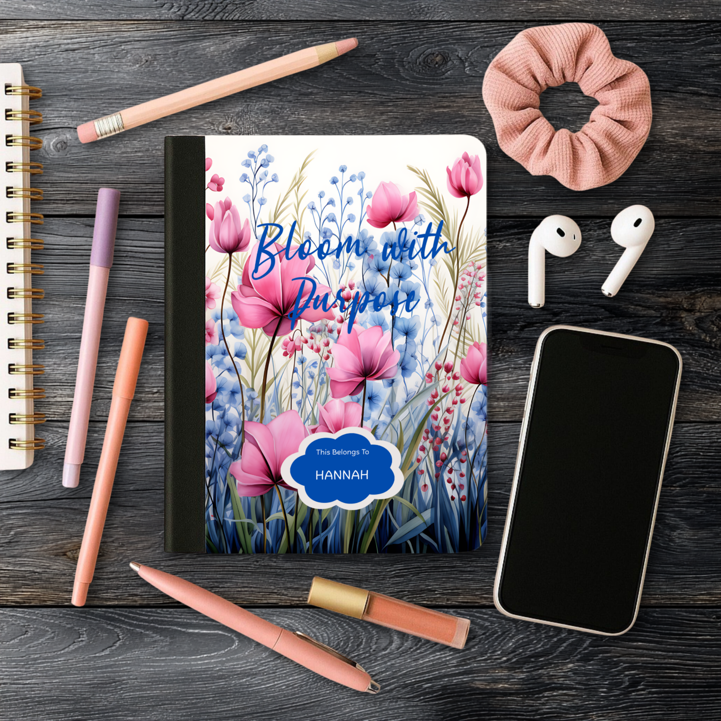 Motivational Journal "Bloom with Purpose" with pink floral cover, personalized name, and surrounding writing accessories on wooden surface