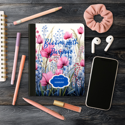 Motivational Journal "Bloom with Purpose" with pink floral cover, personalized name, and surrounding writing accessories on wooden surface