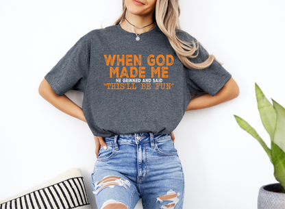 Unisex softstyle t-shirt with "When God Made Me He Grinned and Said This'll Be Fun" orange text, casual religious graphic tee.