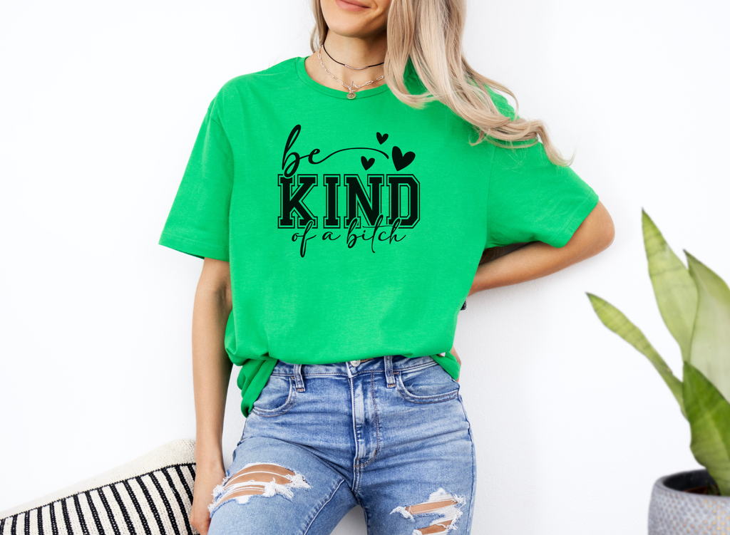 Woman wearing bright green Be Kind of a Bitch softstyle t-shirt with bold black text and hearts, paired with ripped blue jeans