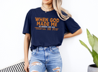 Unisex navy softstyle t-shirt with "When God Made Me He Grinned and Said This'll Be Fun" orange text, casual fit.