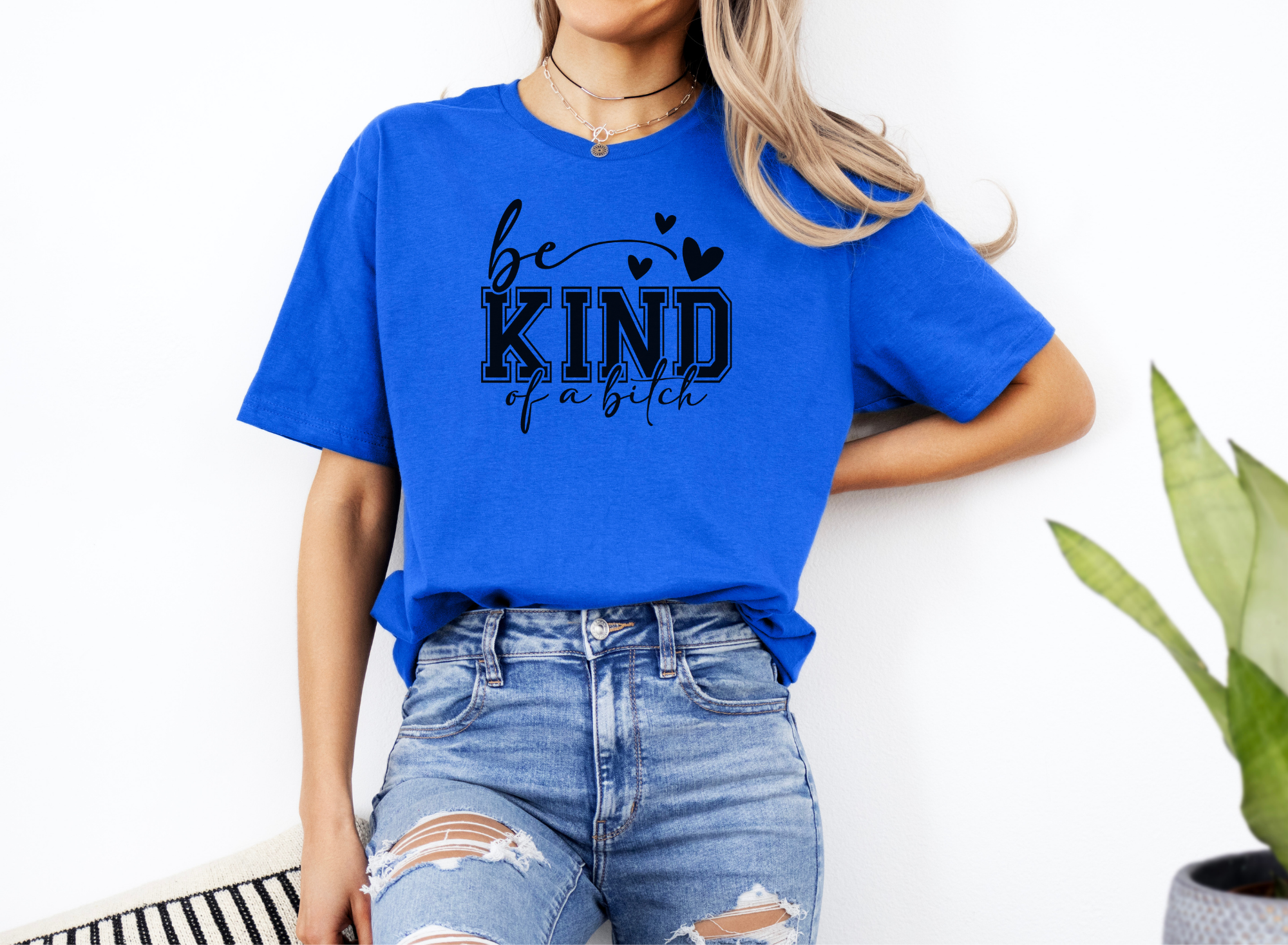 Woman wearing a blue "Be Kind of a Bitch" softstyle t-shirt with black text and heart accents paired with ripped jeans