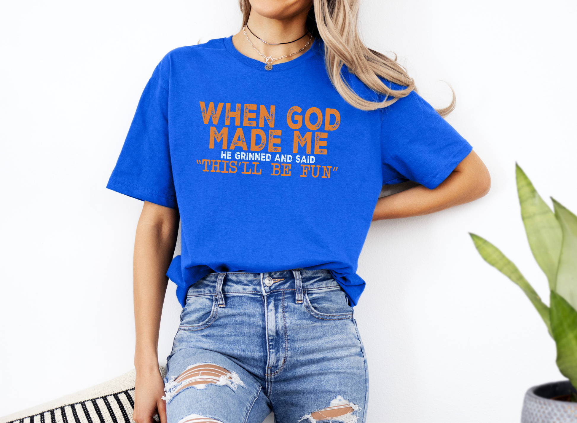 Unisex blue softstyle t-shirt with "When God Made Me He Grinned and Said This'll Be Fun" text, casual fit, paired with ripped jeans