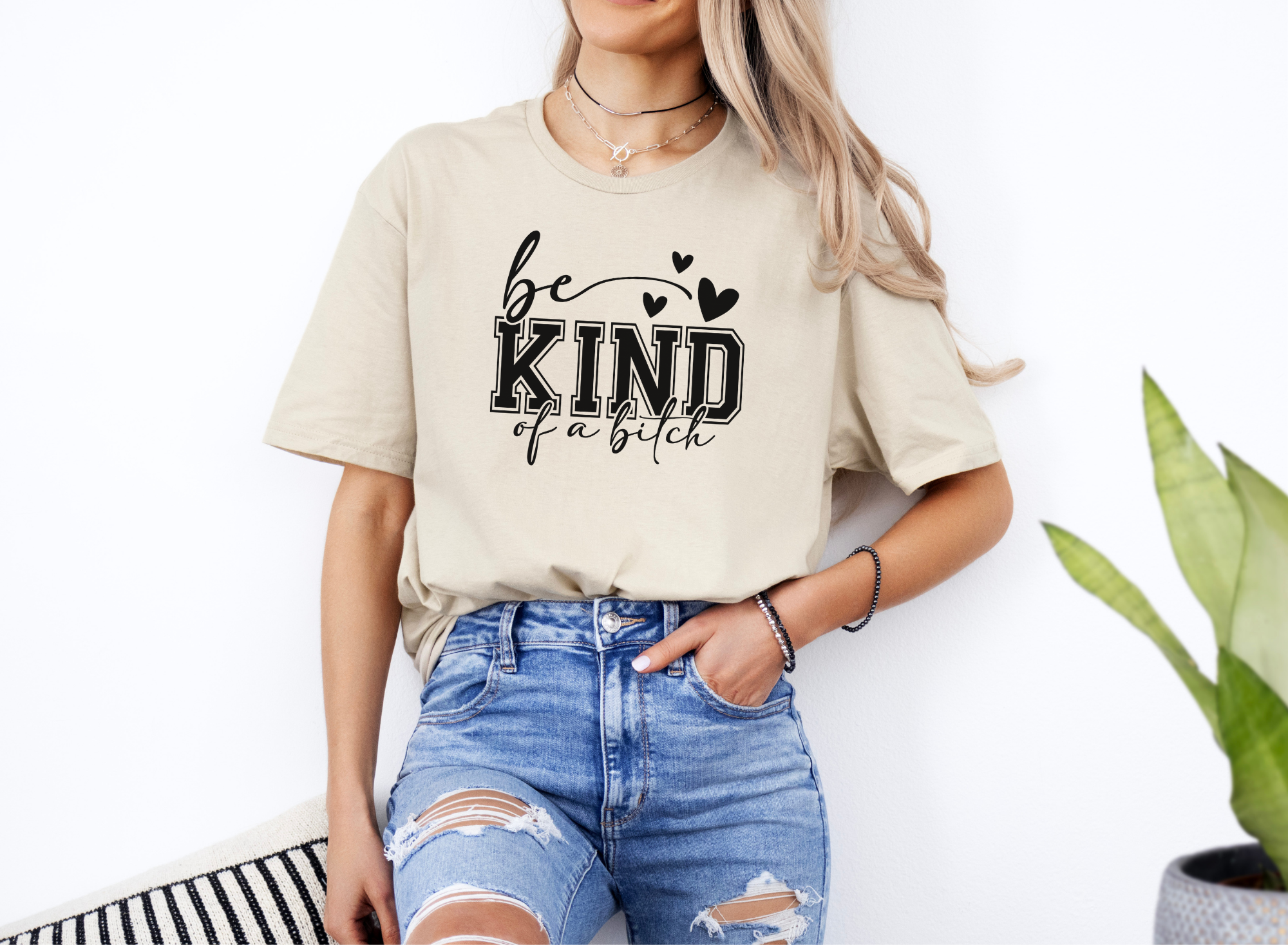woman wearing beige "Be Kind of a Bitch" softstyle t-shirt with black text paired with ripped blue jeans
