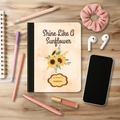Motivational Journal with sunflower design reading Shine Like A Sunflower on desk with pens, pencil, phone, and earbuds