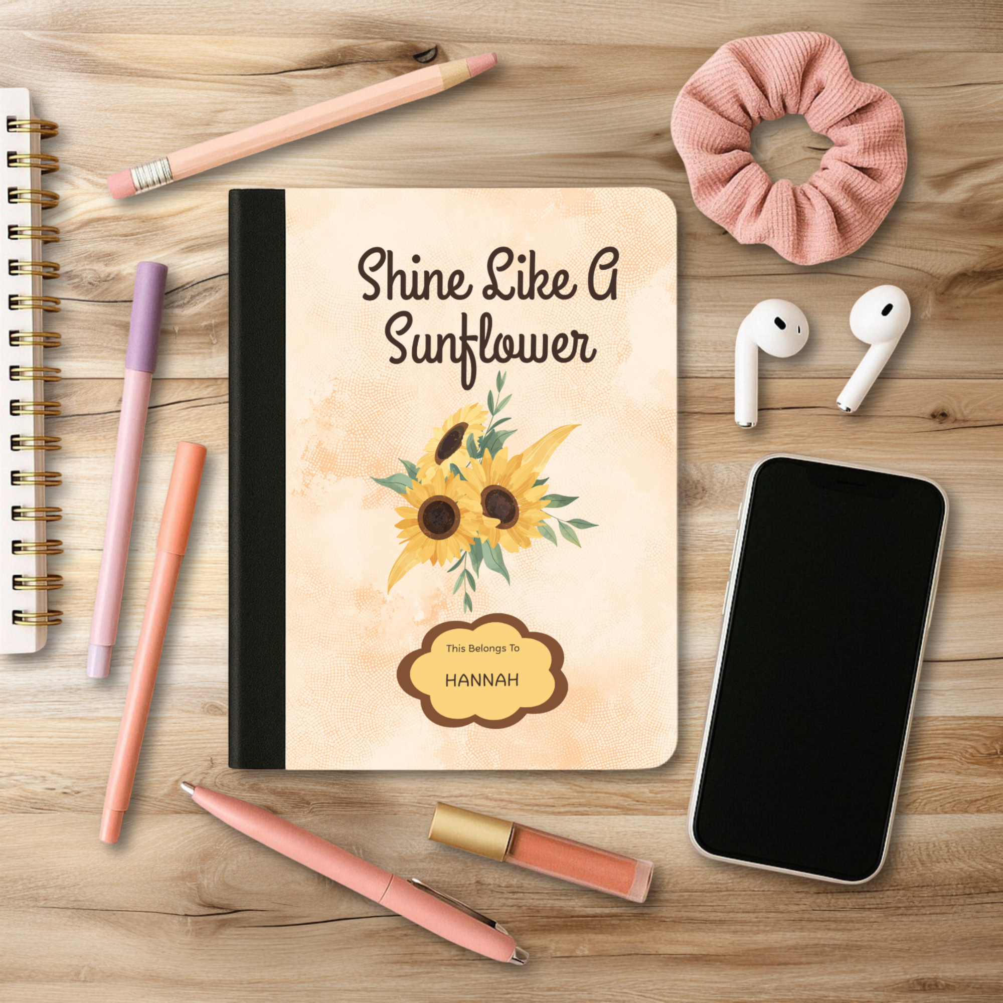 Motivational Journal with sunflower design reading Shine Like A Sunflower on desk with pens, pencil, phone, and earbuds