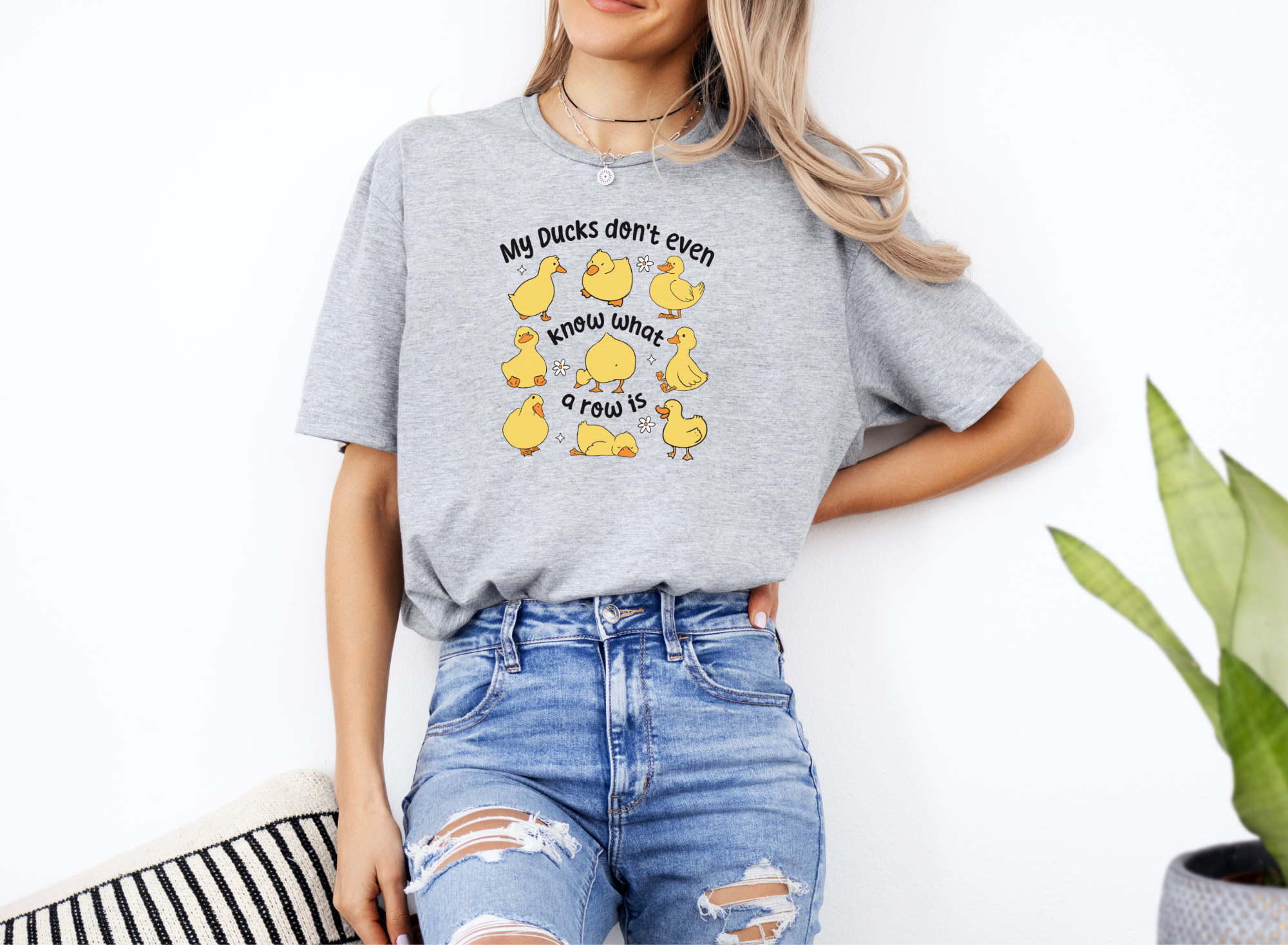 Woman wearing gray Ducks Not In A Row softstyle short sleeve shirt with cartoon ducks illustration and quote.
