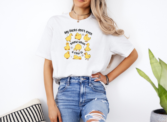 Woman wearing a white Ducks Not In A Row softstyle short sleeve shirt with cartoon yellow ducks and humorous text design.